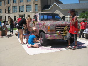 Group of people gathered around a sparkly pick-up truck, decorating it