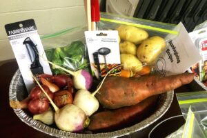 A bin of fresh garden vegetables including turnips, sweet potatoes, potatoes, and onions